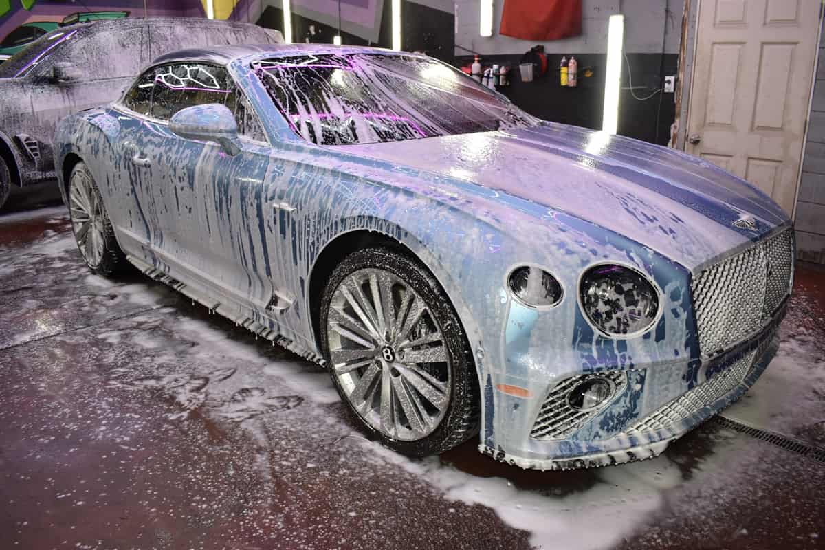 Grand tourer covered in detailing foam inside a lit wash bay