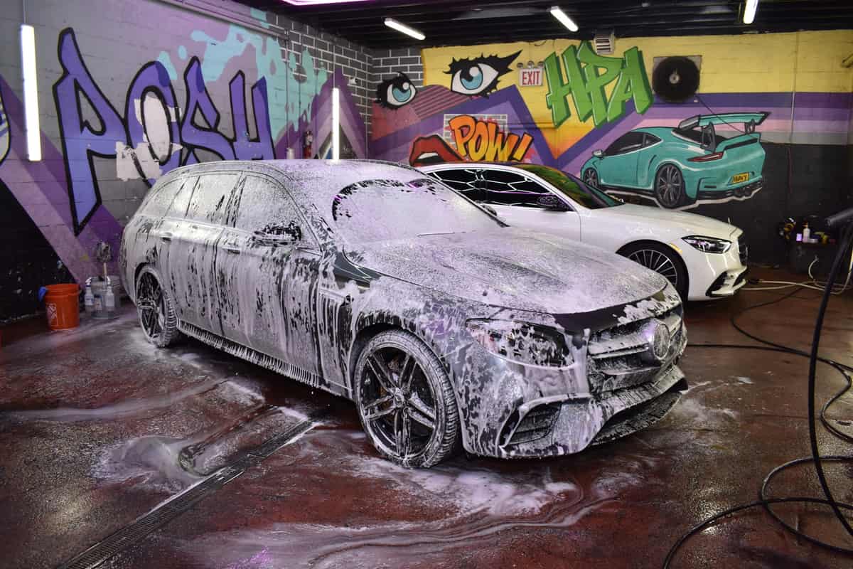 Estate car under a full foam bath in a graffiti-walled detail bay