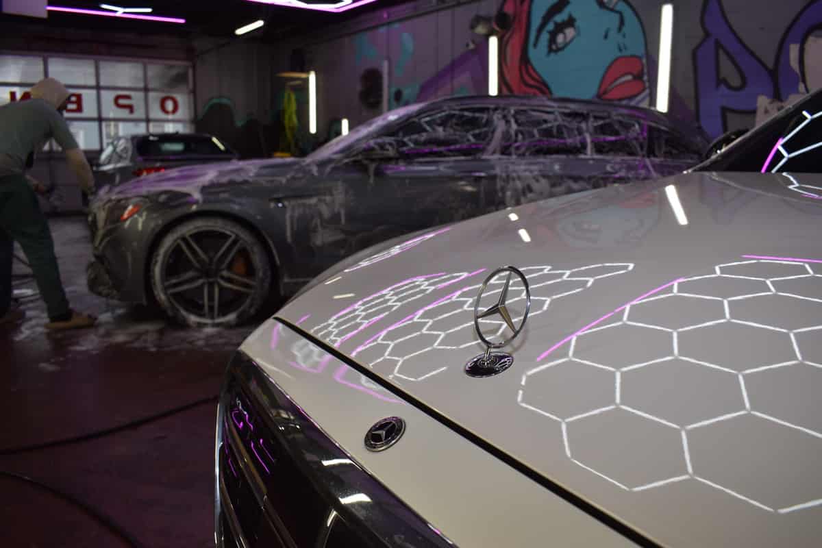 Hexagonal bay lighting reflected across a dark sedan hood