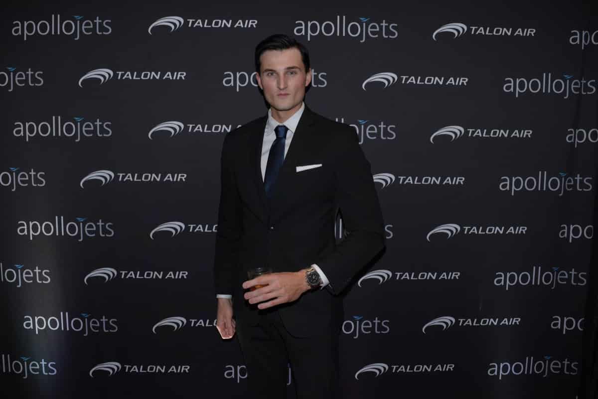 Guest in a tuxedo photographed against a branded aviation step-and-repeat